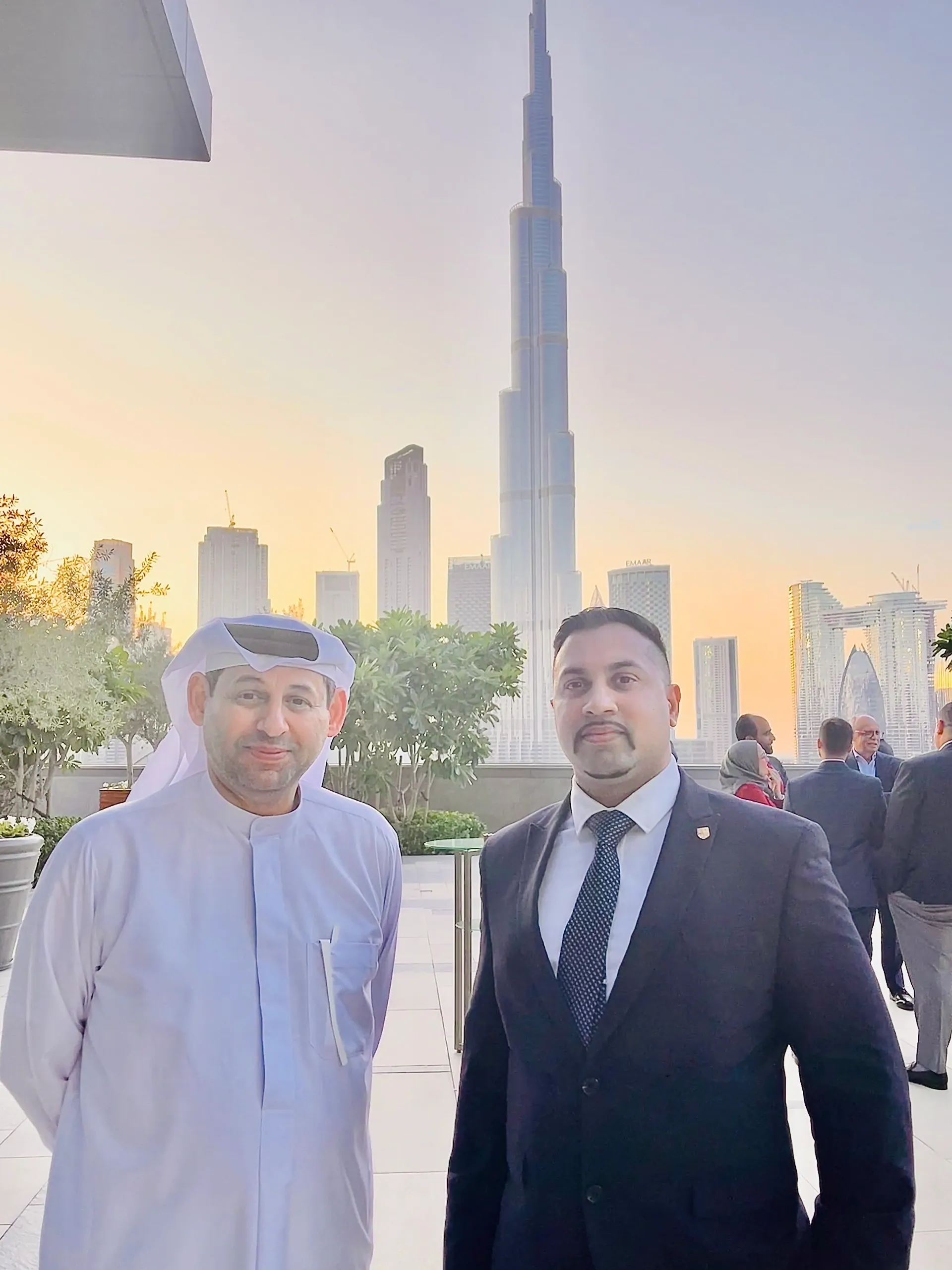 Two men posing with Dubai skyline and Burj Khalifa at sunset.